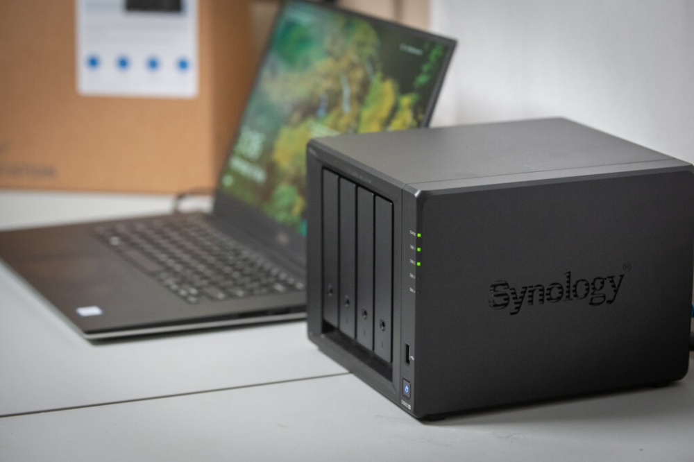 Устройство Synology NAS рядом с ноутбуком с активными LED-индикаторами.