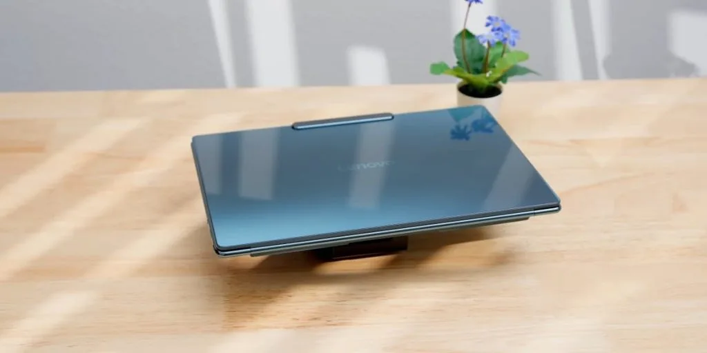 Закрытый ноутбук Lenovo Yoga Slim 9i темно-синего цвета, установленный на подставке на деревянном столе.