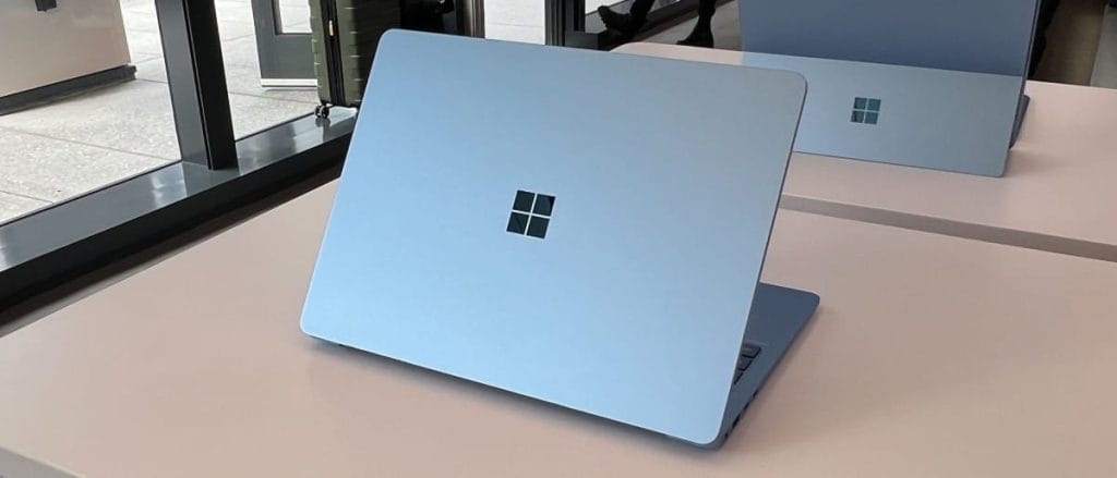 Синий ноутбук Microsoft Surface Laptop 7 с логотипом на крышке, расположенный на столе в современном офисе.