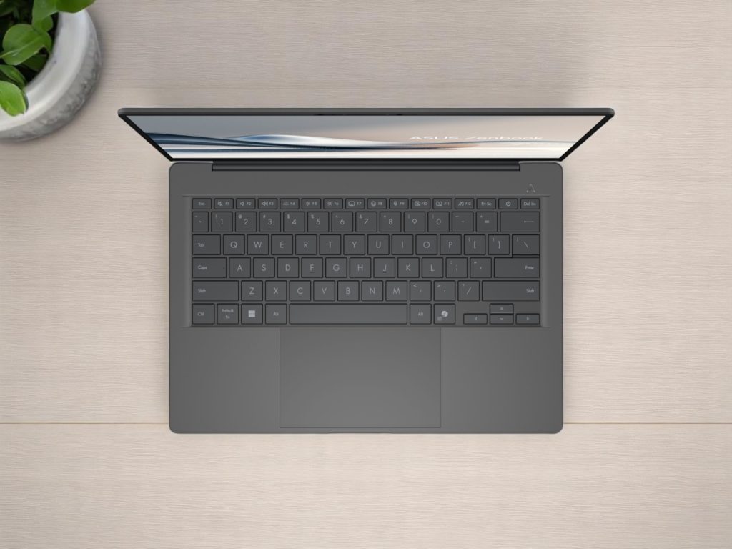 Asus Zenbook A14. Вид сверху на элегантный ноутбук Asus Zenbook с темной клавиатурой на деревянном столе рядом с зеленым комнатным растением
