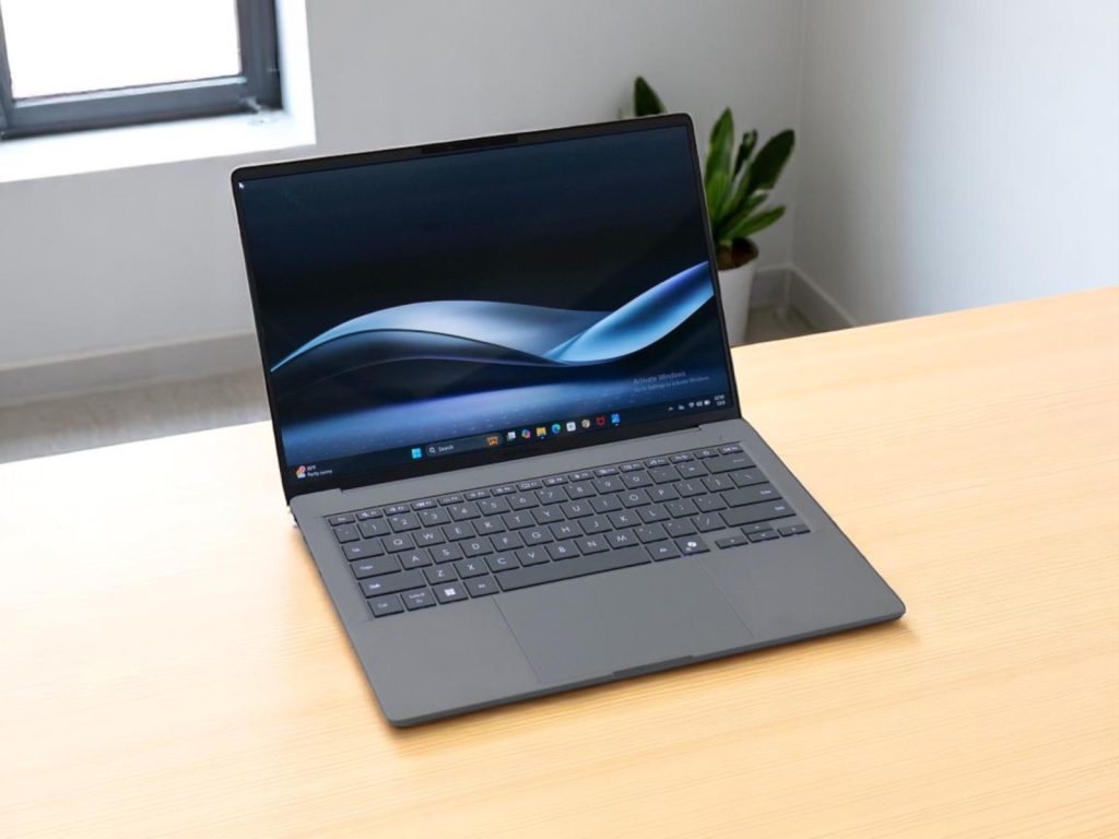 Asus Zenbook A14. Открытый современный ноутбук с элегантным дизайном на деревянном столе у окна и зелёным растением