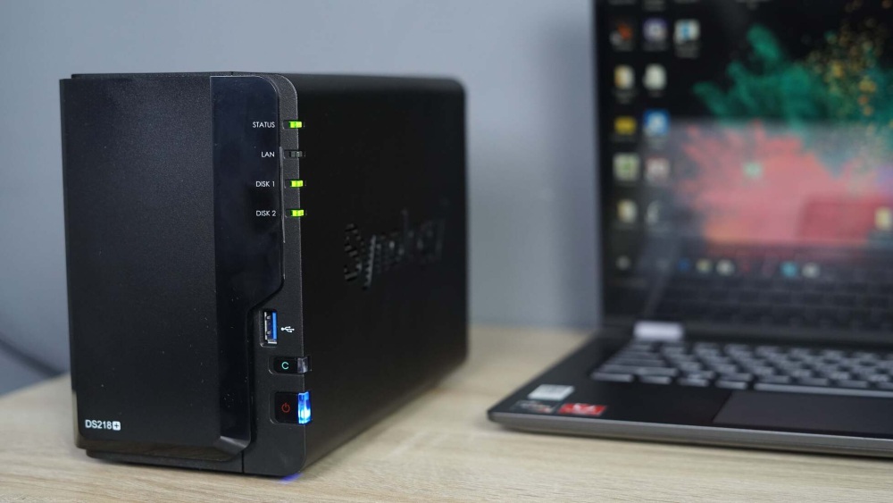 Крупный план Synology NAS с активными LED-индикаторами и ноутбуком на заднем плане.