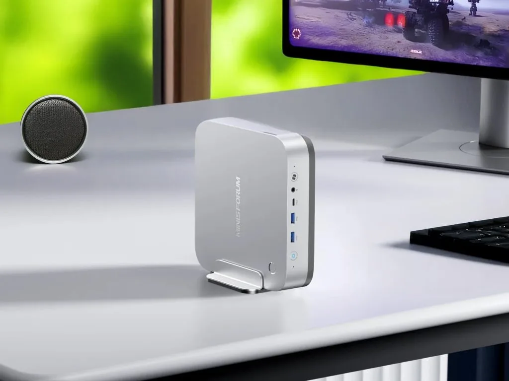 Компактный мини ПК Minisforum AI X1 Pro от MinISFORUM на столе рядом с небольшим динамиком, с монитором, отображающим видеоигру.